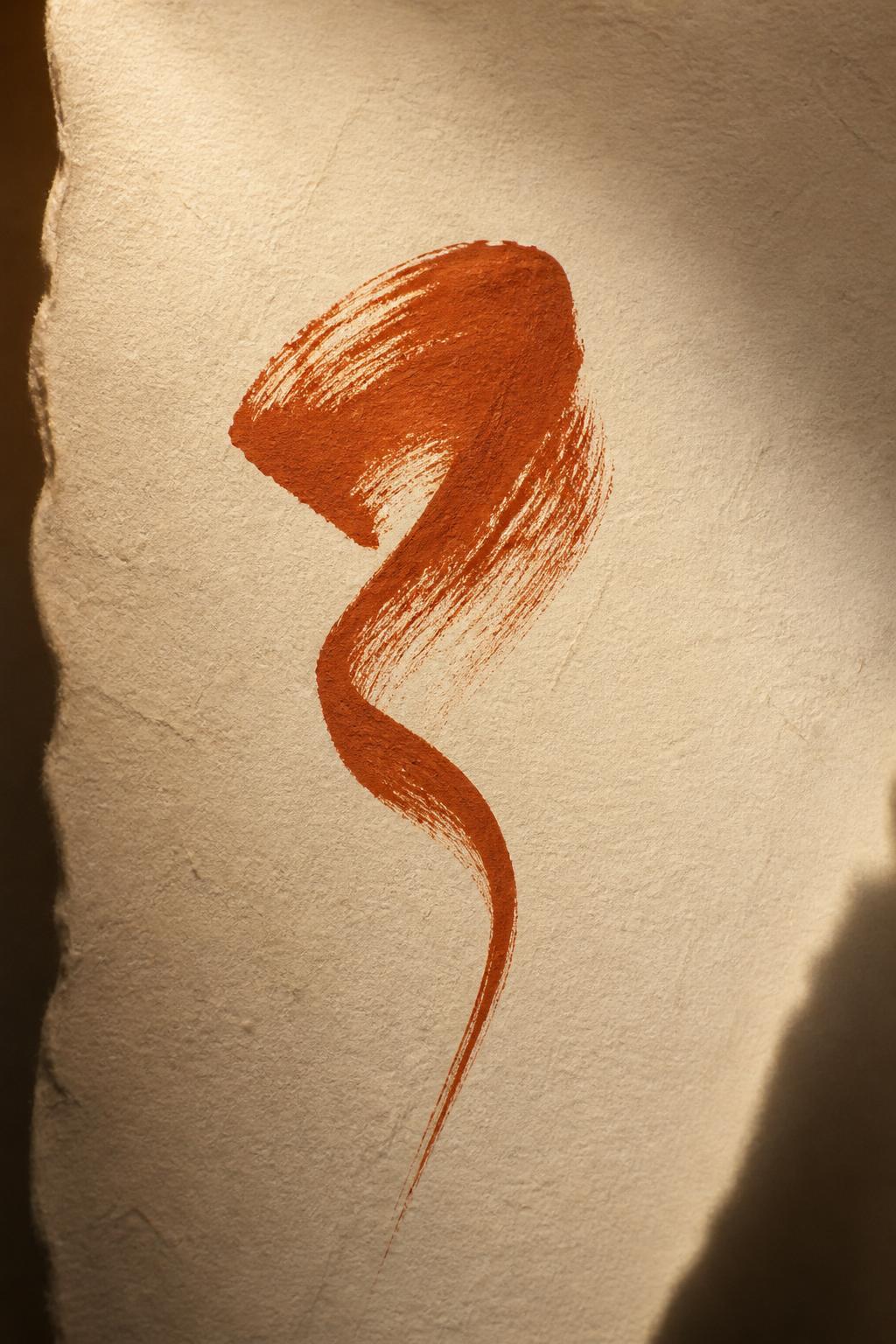 A deliberate terracotta brushstroke pressed into ivory paper